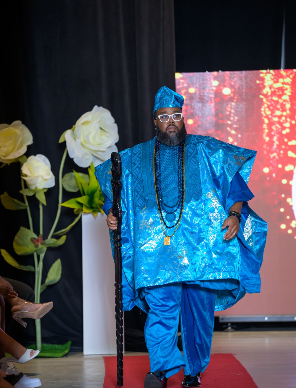 Menswear look in a vivid blue embroidered agbada with beaded necklaces and a carved staff, from the Adeyemi RoyaLabel HIFW Season Six runway