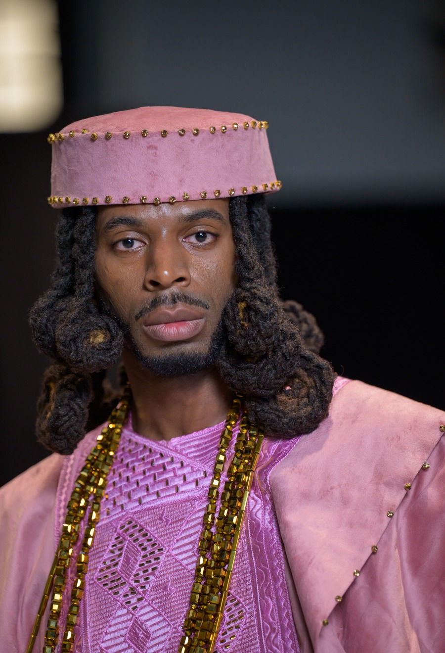 Close-up of a model in pink Adeyemi Royalabel menswear with gold embellishments and a structured cap