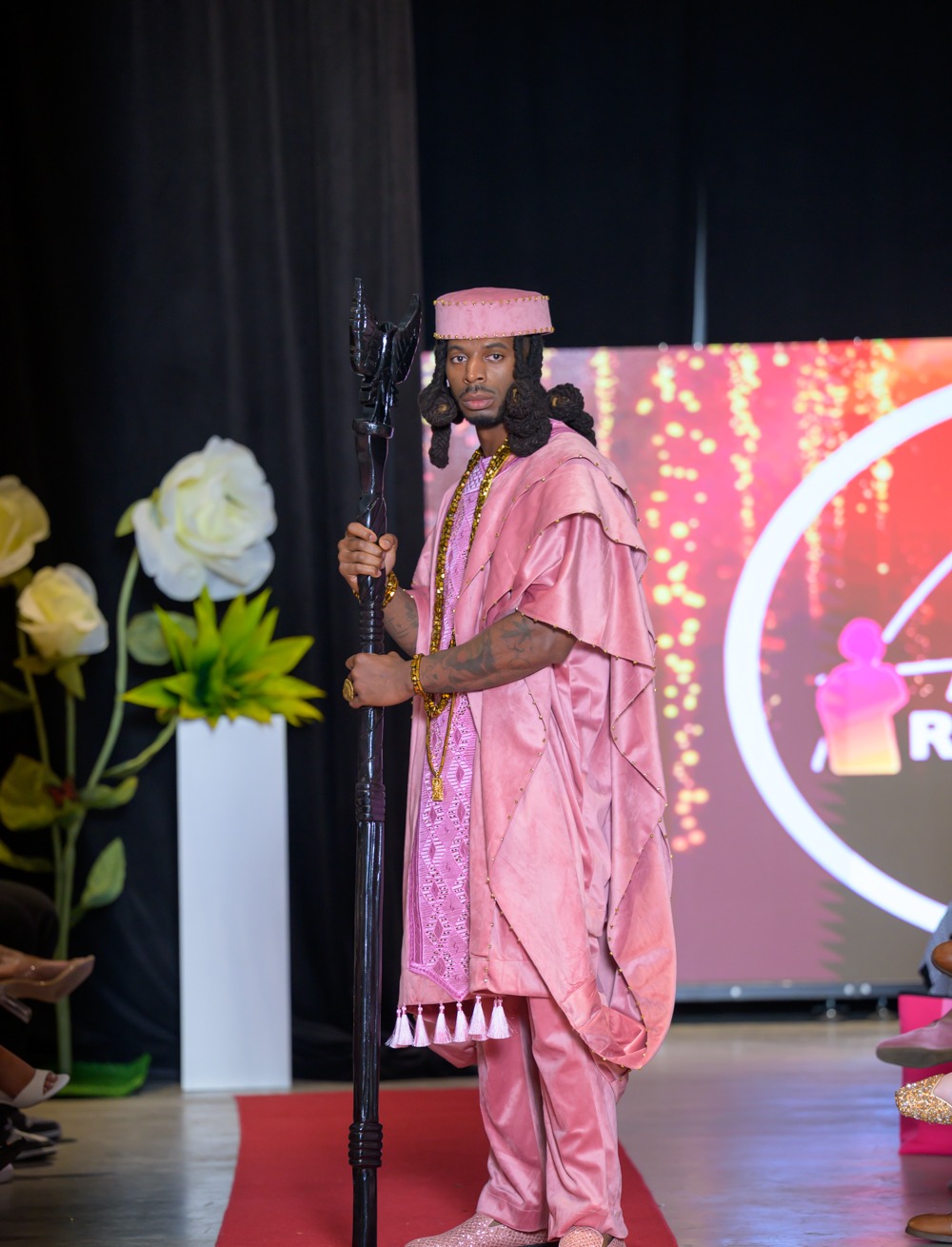 Menswear look in a rose pink layered agbada with beaded detailing, cap and carved staff, from the Adeyemi RoyaLabel HIFW Season Six runway